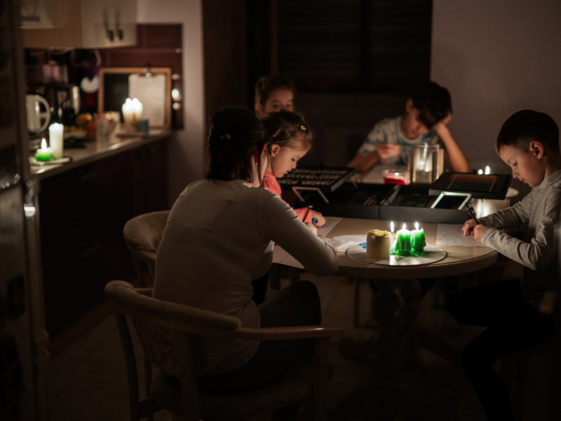 Eine Familie sitzt bei Kerzenschein am Küchentisch und beschäftigt sich während eines Stromausfalls.